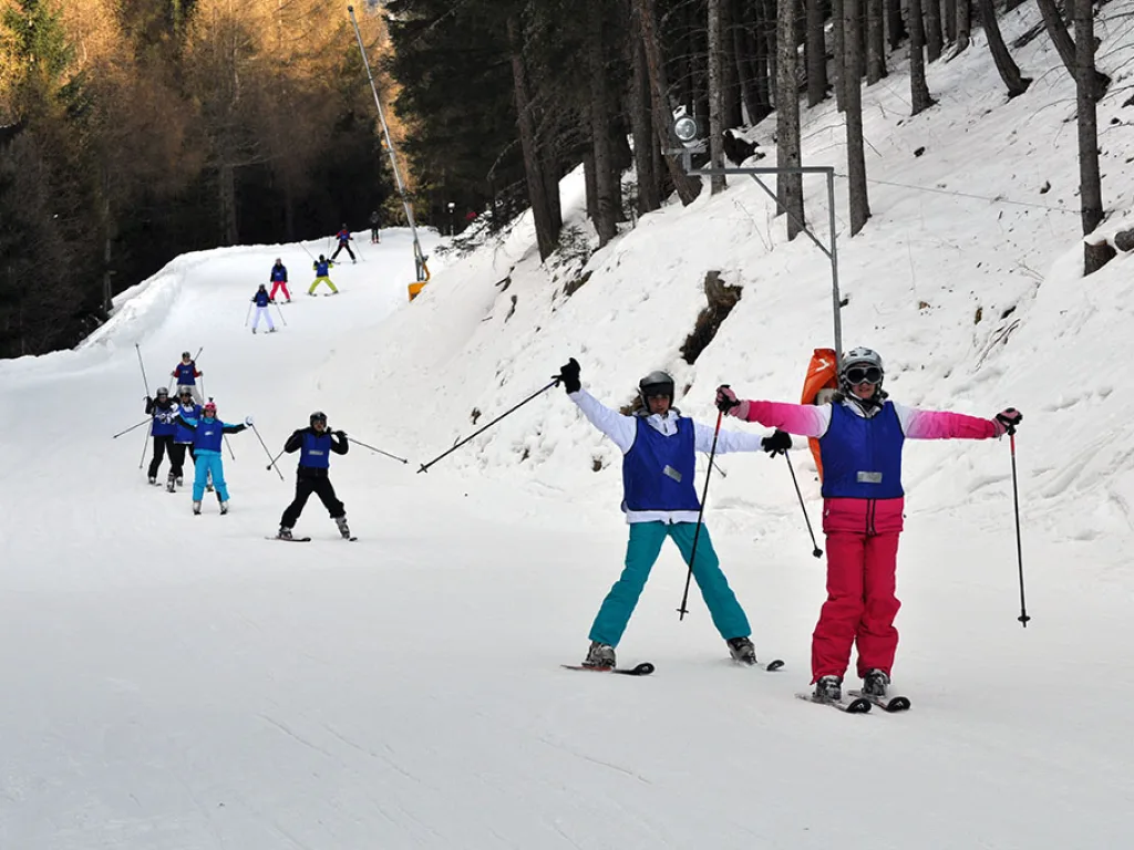 Skifahrende auf einer schmalen Waldpiste, zwei winken.